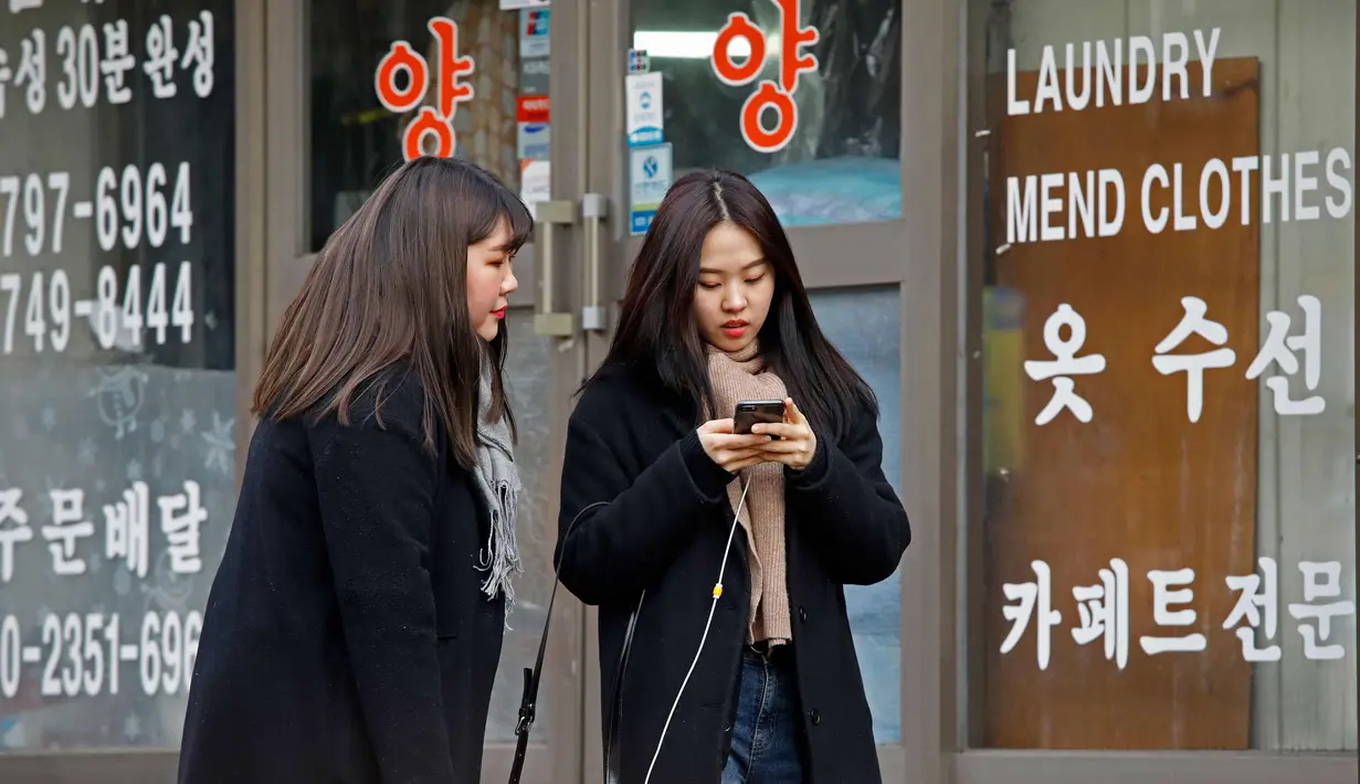 Dua wanita berbincang sambil berjalan di sepanjang jalan di Seoul, Korea Selatan (19/2). (AFP Photo/David Gannon)