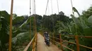 Pengendara motor melintasi jembatan gantung Kuning yang menghubungkan Pasar Minggu Poltangan ke Cililitan Condet, Jakarta, Selasa (28/12/2021). Jembatan gantung dengan panjang 40 meter di atas sungai Ciliwung tersebut baru baru ini dijadikan lokasi foto untuk konten medsos. (merdeka.com/Imam Buhori)
