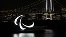 Simbol Paralimpiade menyala pada malam hari dengan latar belakang Jembatan Pelangi di tepi Pantai Odaiba, Tokyo, Jepang, 23 Agustus 2021. Paralimpiade Tokyo 2020 mulai 24 Agustus 2021 sampai 5 September 2021. (Charly TRIBALLEAU/AFP)
