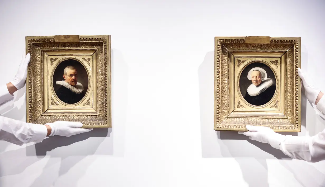 Asisten galeri memegang dua lukisan yang dikaitkan dengan seniman Belanda Rembrandt menjelang presentasi mereka di rumah lelang Christie di Amsterdam pada 21 Juni 2023. Kedua potret itu akan dilelang pada 6 Juli 2023 mendatang, di London. (Kenzo TRIBOUILLARD / AFP)