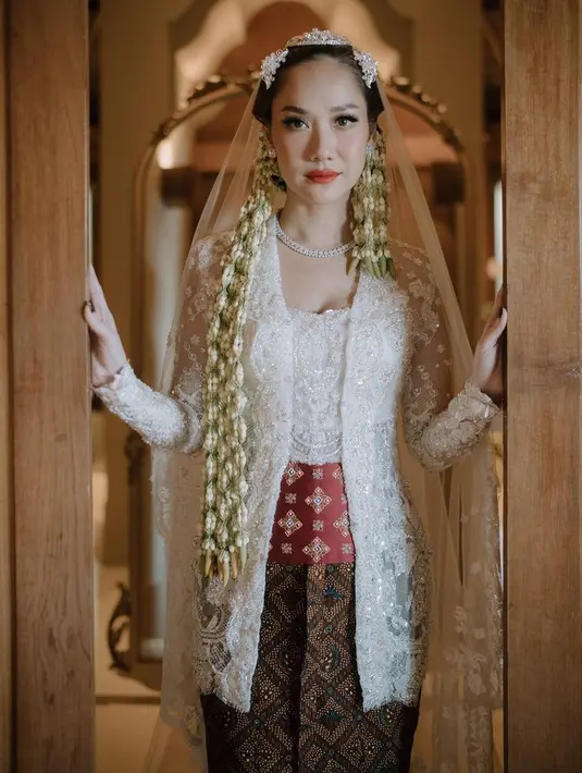 Bunga Citra Lestari tampil dengan kebaya brokat putih model kutu baru saat menikah untuk kedua kalinya. BCL memadukannya dengan obi merah batik dan bawahan kain lilit batik coklat. [@itsmebcl]