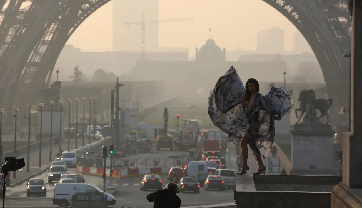 Model seksi ini bergaya di depan menara Eiffel saat matahari terbit dalam sesi pemotretan, Paris (11/3/2016). (AFP/Ludovic MARIN)