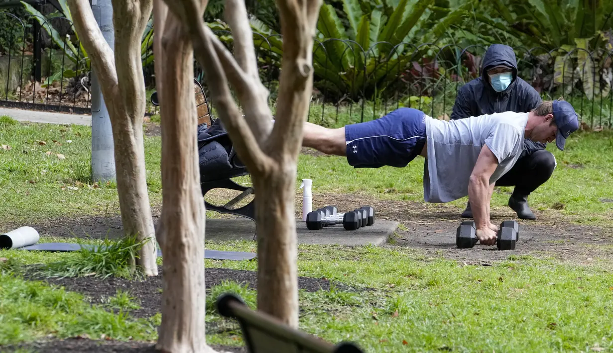 Seorang trainer menyaksikan anggota fitness berolahraga di sebuah taman di pinggiran timur Sydney, pada 14 September 2021. Pelatih pribadi telah mengubah taman kawasan tepi laut di Rushcutters Bay menjadi gym luar ruangan untuk menyiasati pembatasan lockdown karena pandemi covid-19. (AP/Mark Baker)