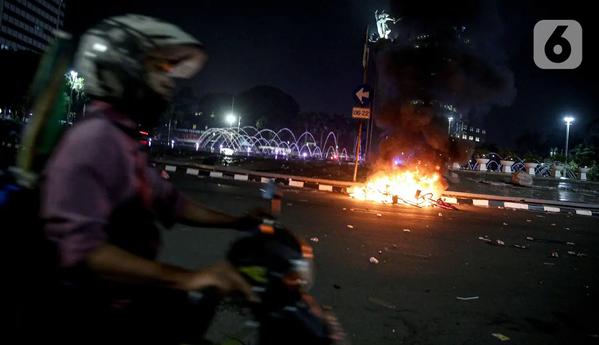 Polisi melintas dekat sejumlah barang yang terbakar usai demonstrasi berujung anarkis di kawasan Bundaran HI, Jakarta, Kamis (8/10/2020). Massa membakar sejumlah barang saat demonstrasi menolak pengesahan UU Cipta Kerja. (Liputan6.com/Faizal Fanani)