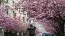 Seorang pria mengambil foto sebuah jalan yang dipenuhi dengan bunga sakura yang mekar di kota Berlin, Jerman pada 23 April 2019. Pohon sakura di Jerman memang lazim ditanam di ruang-ruang terbuka hijau, selain sebagai peneduh juga untuk mempercantik kota. (John MACDOUGALL / AFP)