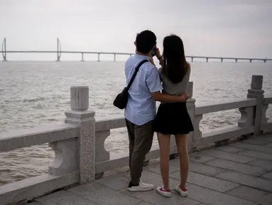 Pasangan mengabadikan Jembatan Hong Kong-Zhuhai-Makau (HKZM) di Zhuha (22/10). Jembatan laut terpanjang di dunia yang menghubungkan Hong Kong, Makau, dan daratan Cina ini akan dibuka untuk lalu lintas pada 24 Oktober 2018. (AFP Photo/Fred Dufour)