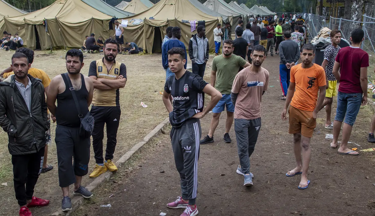 Para migran berjalan di dalam kamp pengungsi yang baru dibangun di tempat latihan militer Rudninkai, sekitar 38km (23,6 mil) selatan dari Vilnius, Lituania, Rabu (4/8/2021). (AP Photo/Mindaugas Kulbis)