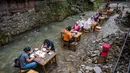 Pelanggan menikmati makan siang di sebuah restoran dengan meja yang berada di tengah aliran sungai di Kampung Kemensah di pinggiran Kuala Lumpur, Malaysia, Selasa (14/7/2020). Tak perlu khawatir, air sungai yang datang dari bukit ini masih bersih dan menyegarkan. (Photo by Mohd RASFAN / AFP)