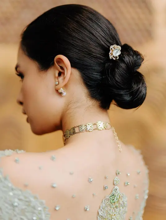 Gaya rambut sanggul rendah yang ditata sleek tanpa poni, ditambah aksesoris tusuk sanggul akan memberi kesan tampilan yang anggun. [@maudyayunda]