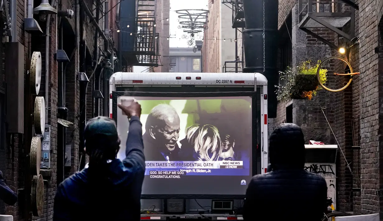 Direktur eksekutif Peace Peloton Doc Wilson (kiri) mengangkat secangkir kopi sebagai penghormatan saat melihat pelantikan Presiden Joe Biden di layar video di Seattle (20/1/2021). Joe Biden mengalahkan Donald Trump di pemilu AS 2020 dengan perolehan 81 juta suara. (AP Photo/Elaine Thompson)