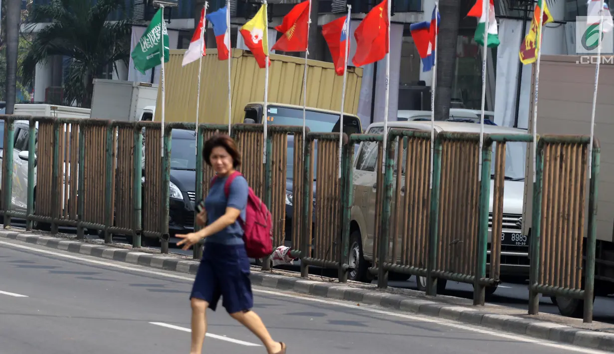 Pejalan kaki menyeberang dekat bendera negara peserta Asian Games 2018 yang diikat di tiang bambu di pagar pembatas Jalan Pluit Selatan Raya, Jakarta, Kamis (19/7). Pemasangan itu inisiatif warga dalam memeriahkan Asian Games. (Liputan6.com/Arya Manggala)