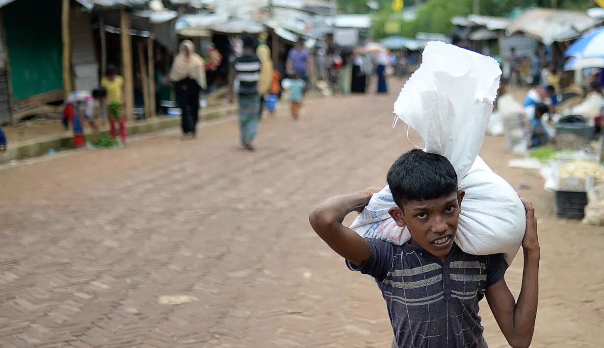 Seorang anak Rohingya membawa bantuan di kamp pengungsi Kutupalong, di Ukhia, Bangladesh pada 6 Oktober 2020. Lebih dari satu juta etnis Rohingya melarikan diri dari Myanmar dan menetap di Kutupalong yang merupakan salah satu kamp pengungsi terbesar di dunia. (Munir Uz Zaman/AFP)