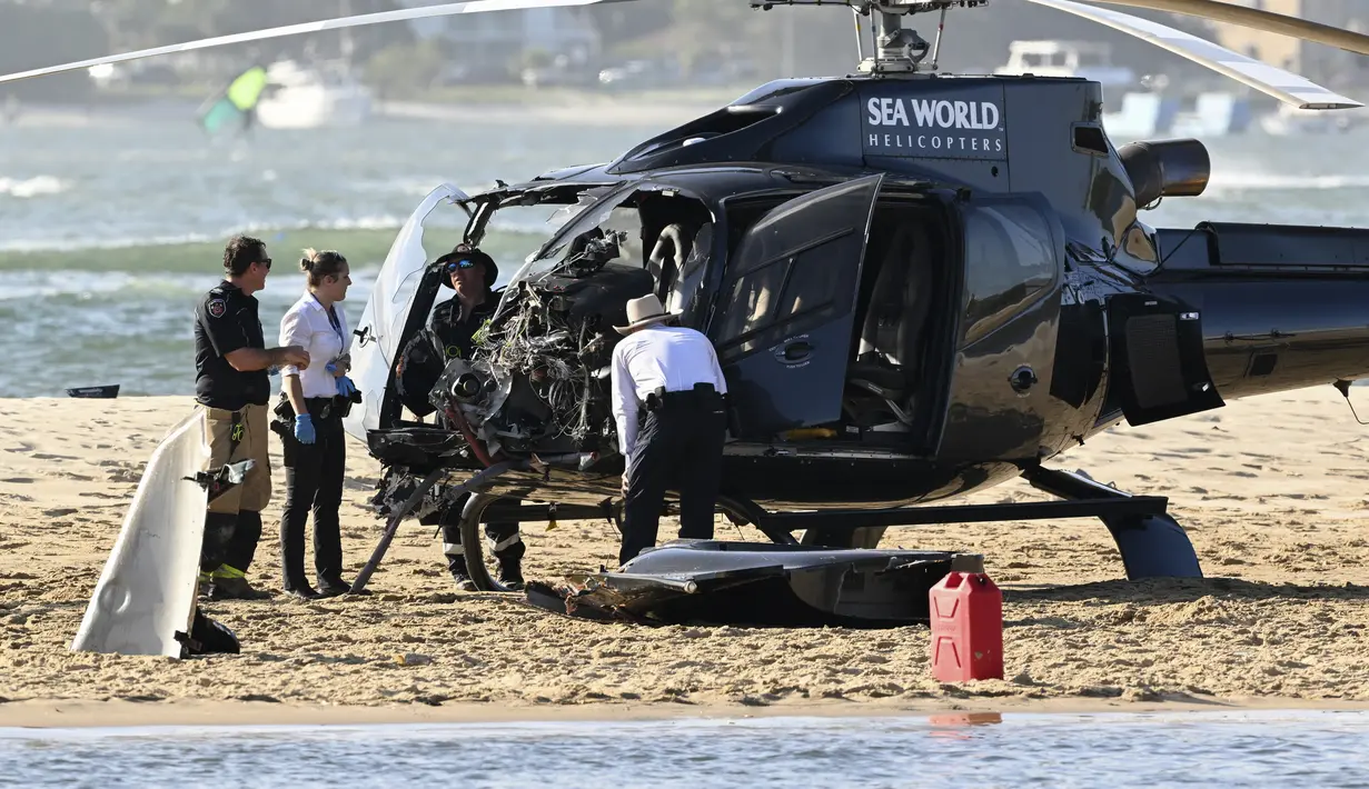 Petugas darurat memeriksa helikopter di lokasi tabrakan dekat Seaworld, di Gold Coast, Australia, Senin, 2 Januari 2023. Dua helikopter bertabrakan di udara menewaskan empat orang termasuk sepasang suami istri dari Inggris dalam kecelakaan yang menarik bantuan darurat dari pengunjung pantai selama musim panas. (Dave Hunt/AAP Image via AP)