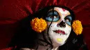 Peserta berdandan menyerupai wanita kerangka menunggu dimulainya Prosesi Grand Catrinas bagian dari perayaan Day of The Dead di Mexico City, Minggu (22/10). Banyak orang yang mengenakan kostum dan hiasan tengkorak memenuhi jalanan. (AP/Rebecca Blackwell)