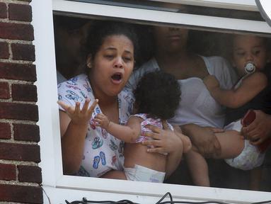 Wanita menggendong bayi menunggu bantuan setelah kebakaran terjadi di dalam gedung apartemen di Hazleton, Pennsylvania (26/7/2019). Pemadam kebakaran kota menggunakan truk menyelamatkan penghuni dari lantai tiga gedung. (Warren Ruda/Hazleton Standard-Speaker via AP)