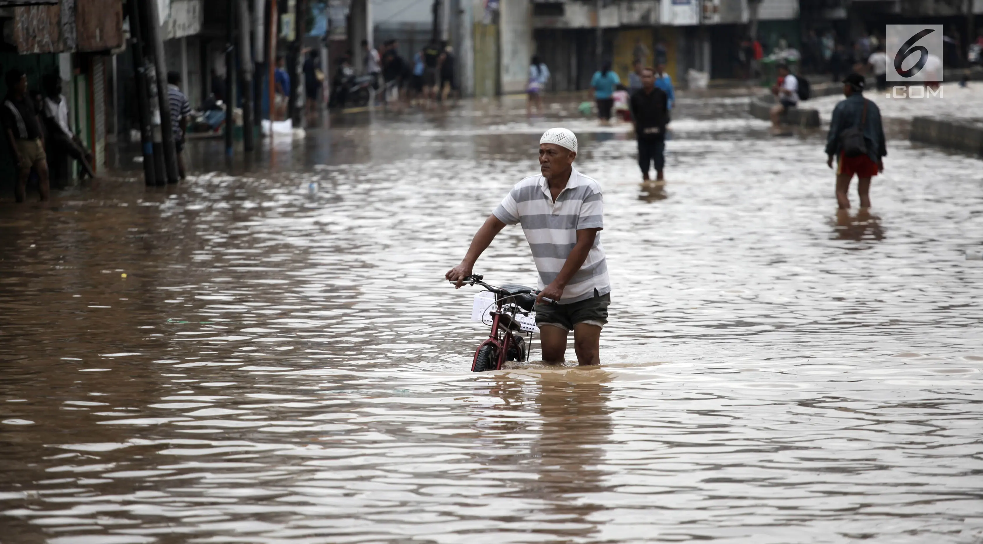 Seorang pria berjalan bersama sepedanya melintasi banjir di Jalan Jatinegara Barat, Jakarta Timur, Selasa (6/2). Genangan tersebut membuat lalu lintas Jalan Jatinegara Barat terputus. (Liputan6.com/Arya Manggala)