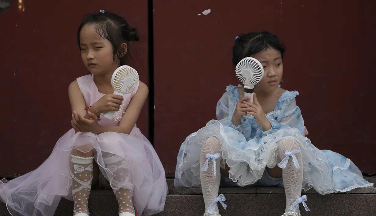 <p>Anak-anak mendinginkan diri dengan kipas angin listrik saat beristirahat dekat Kota Terlarang pada hari yang panas di Beijing, China, 25 Juni 2023. Beijing meningkatkan level peringatan cuaca panas menjadi level tertinggi, yaitu kode merah. (AP Photo/Andy Wong)</p>