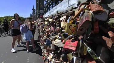 Kaum muda memeriksa gembok cinta di sebuah jembatan di Cologne, Jerman, Rabu, (5/8/2020). Sebagai bukti cinta mereka, puluhan ribu pasangan telah memasang gembok selama bertahun-tahun ke pagar di Jembatan Hohenzollern sebelum melempar kunci ke sungai Rhein di bawah. (AP Photo/ Martin Meissner)