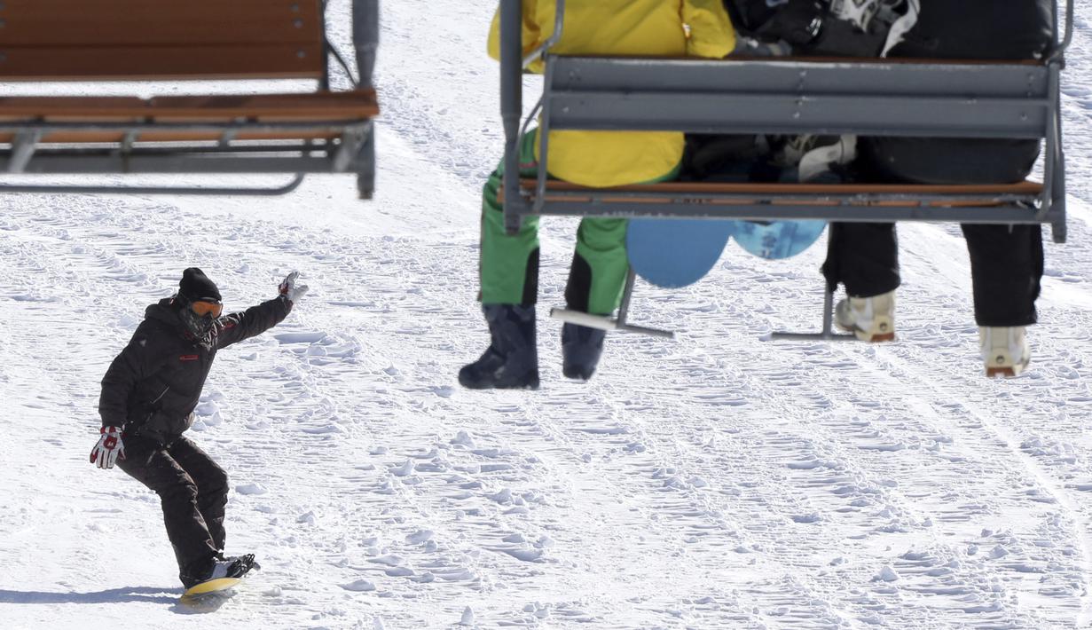 Pemain snowboard menuruni lereng saat dua orang lainnya duduk di kursi gantung di resor ski Tochal di kota Teheran, Iran (1/1/2022). Di tengah polusi udara dan kesengsaraan ekonomi, penduduk Teheran menemukan kenyamanan di resor ski di utara Teheran di pegunungan Alborz. (AP Photo/Vahid Salemi)