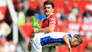 Bek Manchester United, Harry Maguire, mengangkat kaki pemain Brighton and Hove Albion, Leandro Trossard, pada laga Liga Inggris di Stadion Old Trafford, Minggu (07/08/2022). (AP/Lindsey Parnaby)