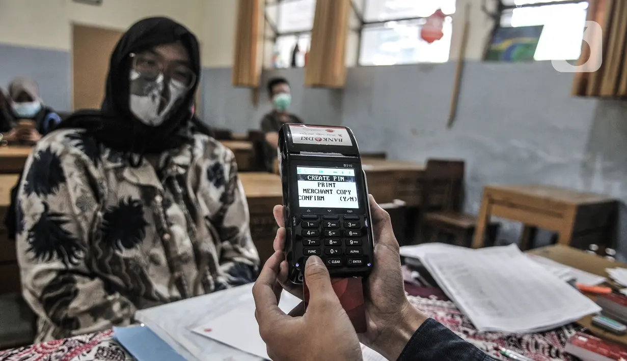 Petugas mengaktifkan kartu ATM Bank DKI warga penerima BST di SMPN 3, Jakarta, Selasa (26/1/2021). Pencairan BST di Jakarta yang dilakukan Bank DKI bersama Dinsos DKI Jakarta dibatasi hanya 500 orang penerima per titik per hari demi menghindari penyebaran COVID-19. (merdeka.com/Iqbal S. Nugroho)