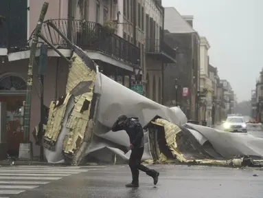 Seorang pria melewati bagian dari sebuah bangunan di French Quarter yang terjatuh dan menutup jalan akibat tertiup angin saat badai Ida menerpa kawasan New Orleans, Minggu (29/8/2021). Badai topan Ida mulai melanda daratan wilayah selatan Amerika Serikat (AS). (AP Photo/Eric Gay)