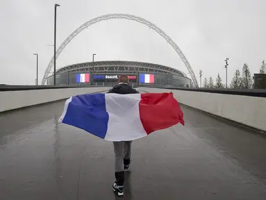 Seorang suporter Prancis membawa bendera Prancis saat menuju Stadion Wembley, London, jelang pertandingan persahabatan antara Inggris melawan Prancis, Selasa (17/11/2015). (AFP Photo/Justin Tallis)