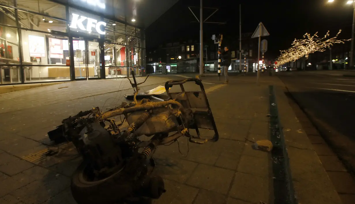 Skuter yang terbakar tergeletak di trotoar di luar restoran cepat saji yang hancur sebagai protes terhadap jam malam nasional di Rotterdam, Belanda, Senin (25/1/2021). Mulai 23 Januari, jam malam dimulai di Belanda dari pukul 21.00 hingga 04.30 untuk mengendalikan COVID-19. (AP Photo/Peter Dejong)