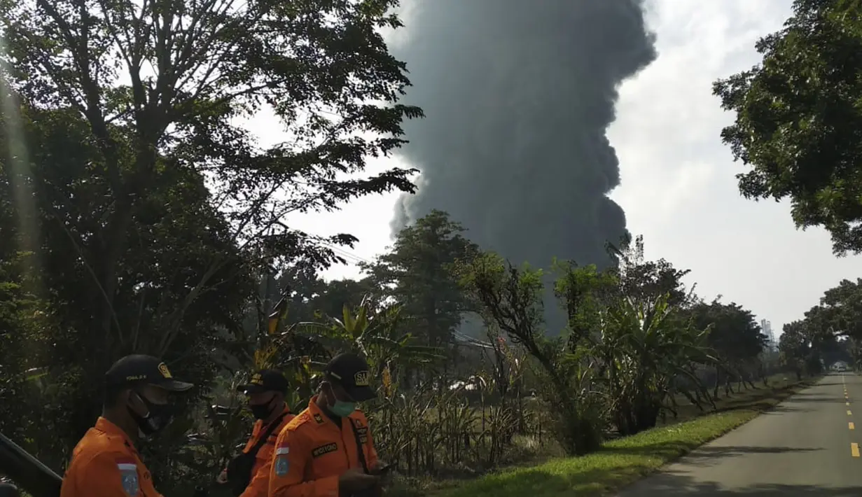 Petugas penyelamat berdiri saat asap tebal mengepul dari api yang melanda Kilang Pertamina Balongan di Indramayu, Jawa Barat, Indonesia, Senin (29/3/2021). Ratusan orang yang tinggal di desa-desa sekitar kilang telah dievakuasi menyusul kebakaran yang terjadi setelah kebakaran. (AP Photo)