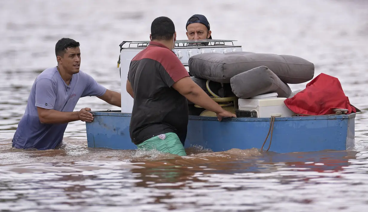 Orang-orang mengarungi air saat mereka memindahkan barang-barang dari rumah mereka yang terendam banjir di negara bagian Minas Gerais di kotamadya Juatuba, Brasil (10/1/2022). Hujan deras yang turun dalam beberapa hari terakhir di bagian tenggara negara itu membuat banjir besar. (AFP/Douglas Magno)