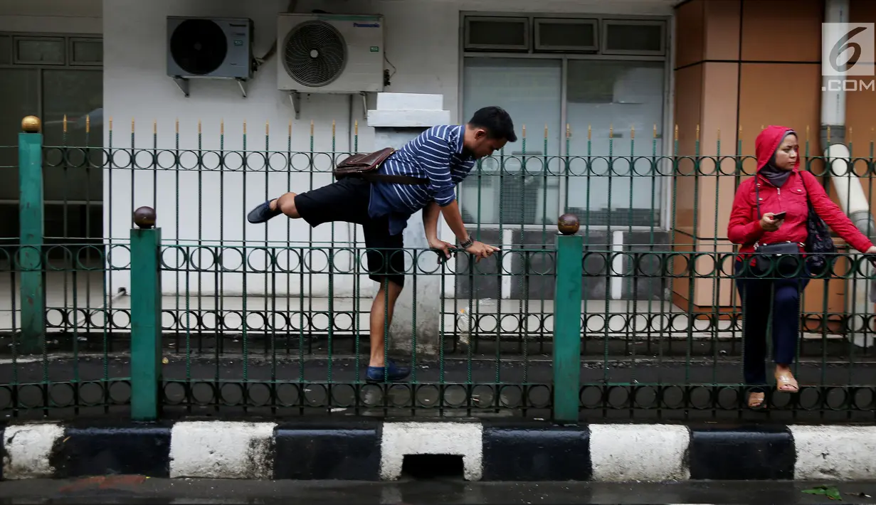 Seorang pria melompati pagar pembatas di Stasiun Cikini, Jakarta Pusat, Rabu, (20/12). Akses pintu keluar stasiun yang terlalu jauh membuat banyak penumpang yang mencari jalan pintas dengan melompat pagar satsiun. (Liputan6.com/Johan Tallo)