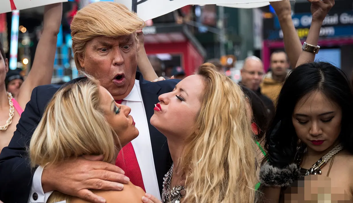 Seorang seniman berpenampilan seperti kandidat presiden AS dari Partai Republik Donald Trump melakukan aksi unjuk rasa dengan dikelilingi wanita-wanita seksi berbikini di depan Times Square, New York (25/10). (AFP Photo/Drew Angerer/Getty Images)