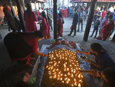 Seorang umat Hindu melakukan ritual dengan berbaring di tempat tidur yang ditutupi dengan 108 lampu minyak menyala pada hari kesepuluh festival Dashain di sebuah kuil di Bhaktapur di pinggiran Kathmandu (15/10/2021). (AFP/Prakash Matematika)
