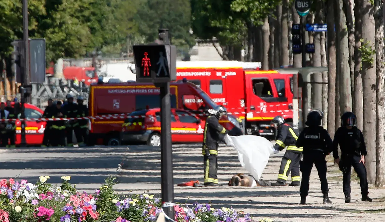 Petugas penyelamat menutupi jasad seorang pria usai menabrakkan mobilnya ke van polisi di jalan Champs Elysees, Paris, Senin (19/6). Belum diketahui pelaku tewas karena hantaman mobil atau tindakan dari polisi. (AP Photo/Thibault Camus)