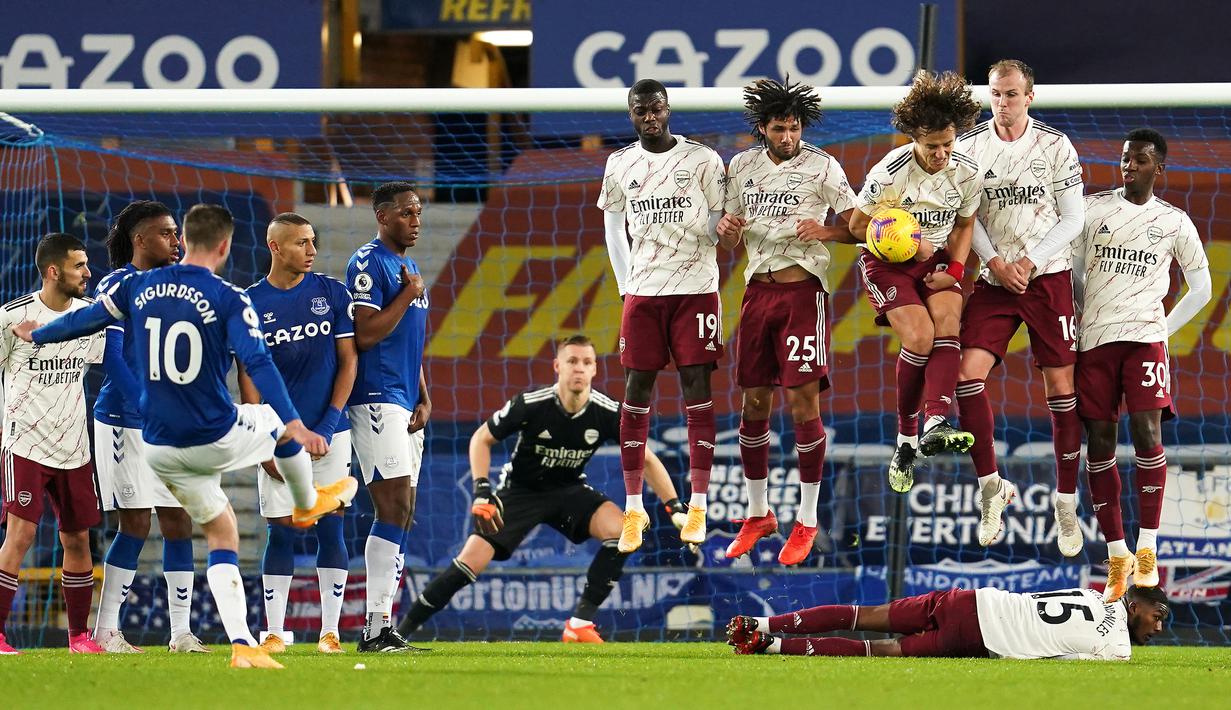 Gelandang Arsenal, Ainsley Maitland-Niles berbaring di belakang rekan-rekannya yang membuat pagar hidup untuk menjaga tendangan bebas yang dilakukan gelandang Everton, Gylfi Sigurdsson dalam laga lanjutan Liga Inggris 2020/21 di Goodison Park, Sabtu (19/12/2020). (AFP/Jon Super/Pool)