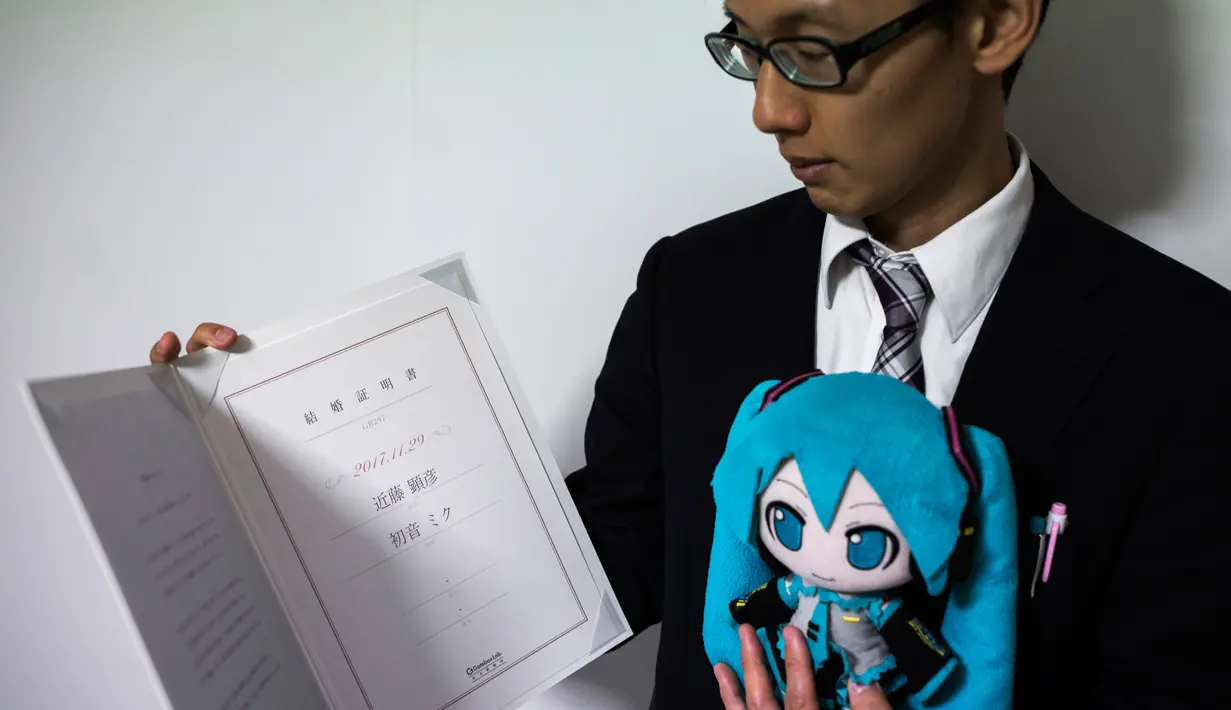 Akihiko Kondo asal Jepang berpose dengan boneka aktris virtual, Hatsune Miku sambil menunjukkan surat nikah mereka di Tokyo, 10 November 2018. Pengalaman traumatis yang 10 tahun lalu membuat pria 35 tahun itu trauma pada wanita. (Behrouz MEHRI/AFP)