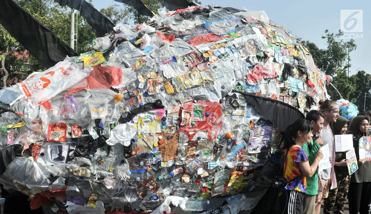 Peserta mengangkat poster dekat instalasi "monster plastik" dalam pawai bebas plastik di Taman Aspirasi Monas, Jakarta, Minggu (21/7/2019). Monster plastik berupa rangka berbentuk menyerupai ikan Angler Fish setinggi 4 meter tersebut dibuat dari 500 kg sampah plastik. (merdeka.com/Iqbal S Nugroho)