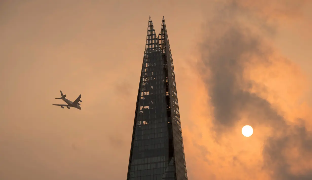 Sebuah pesawat melintas di atas gedung pencakar langit The Shard di pusat kota London, Senin (16/10). Beberapa area menunjukkan langit di London berubah warna menjadi kemerahan, kekuningan, bahkan ada yang kecokelatan. (Dominic Lipinski/PA via AP)