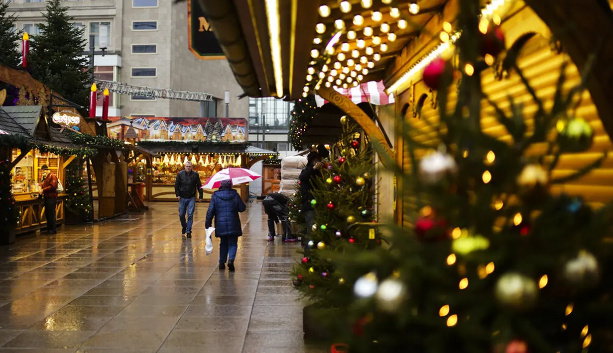 Warga berjalan melintasi Pasar Natal pada pagi yang hujan di Berlin, Jerman, Selasa (30/11/2021). Otoritas Jerman mewajibkan penggunaan masker di transportasi umum dan penumpang perlu divaksinasi, pulih atau negatif COVID-19. (AP Photo/Markus Schreiber)