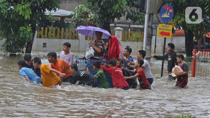 Warga menggunakan jasa gerobak untuk menghindar banjir yang merendam Jalan Pondok Raya Gede, Jakarta Timur, Selasa (25/2/2020).  Sejumlah ruas jalan tergenang dan akses ke beberapa wilayah terputus, salah satunya Jalan Pondok Raya Gede. (Liputan6.com/Herman Zakharia)