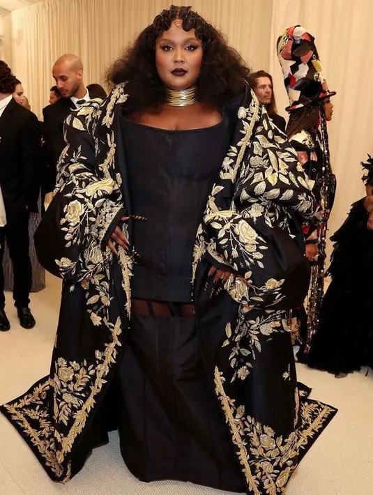 <p>Lizzo tampil begitu glamor dalam balutan dress hitam dan outer dengan aksen bordir emas dari Thom Browne. (Instagram/metgalaofficial).</p>