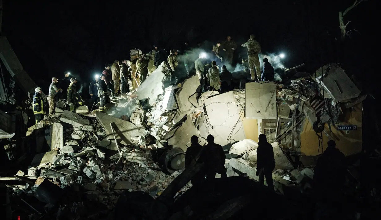 <p>Tim penyelamat memindahkan puing-puing untuk mencari korban selamat di gedung apartemen yang hancur terkena roket pada malam hari di pusat kota Kramatorsk, Ukraina timur, pada Rabu (1/2/2023). Laporan kepolisian juga menyebut serangan dilancarkan dengan rudal jenis 'Iskander-K'. (Yasuyoshi CHIBA / AFP)</p>