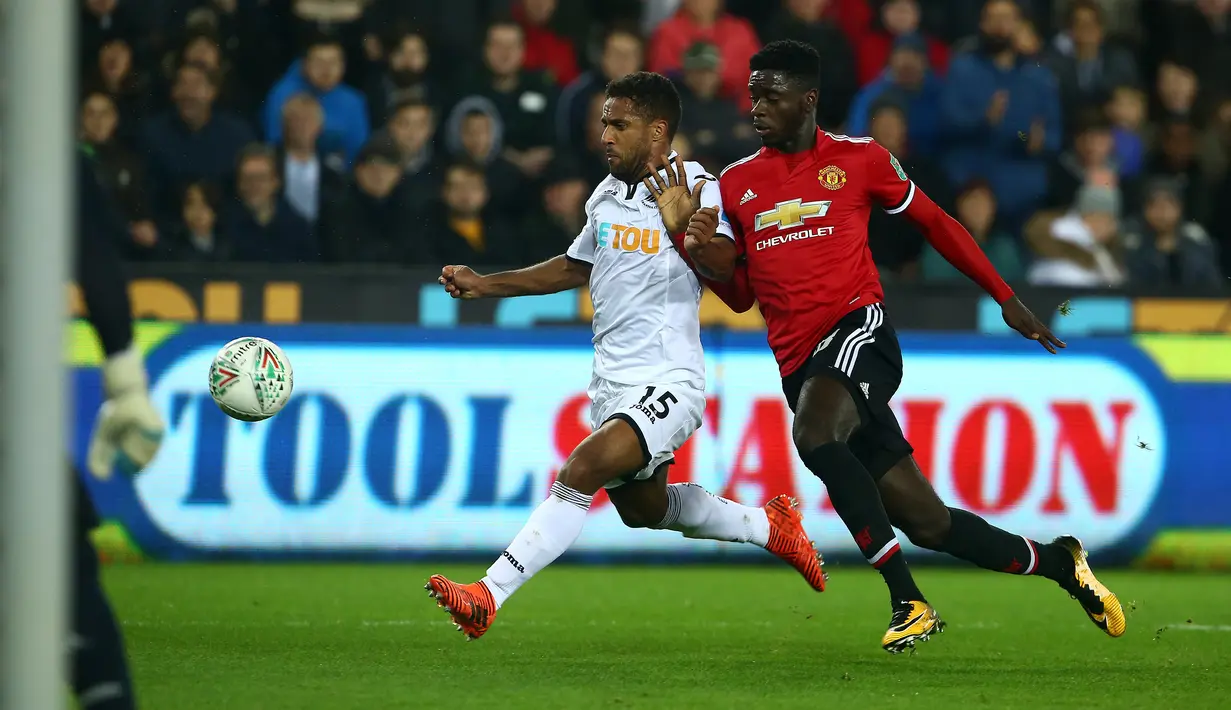 Pemain Manchester United, Axel Tuanzebe berebut bola dengan gelandang  Swansea City, Wayne Routledge pada pertandingan Piala Liga Inggris di Liberty Stadium, Rabu (25/10). MU sukses menekuk Swansea City dengan skor 2-0. (GEOFF CADDICK/AFP)