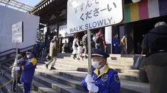 Penjaga keamanan memegang tanda untuk mengontrol pengunjung yang berjalan untuk berdoa memohon keberuntungan selama "hatsumode" atau kunjungan pertama tahun ini ke kuil atau wihara, di kuil Kawasaki Daishi di Kawasaki, dekat Tokyo, Senin, 2 Januari 2023. (AP Photo/Eugene Hoshiko)