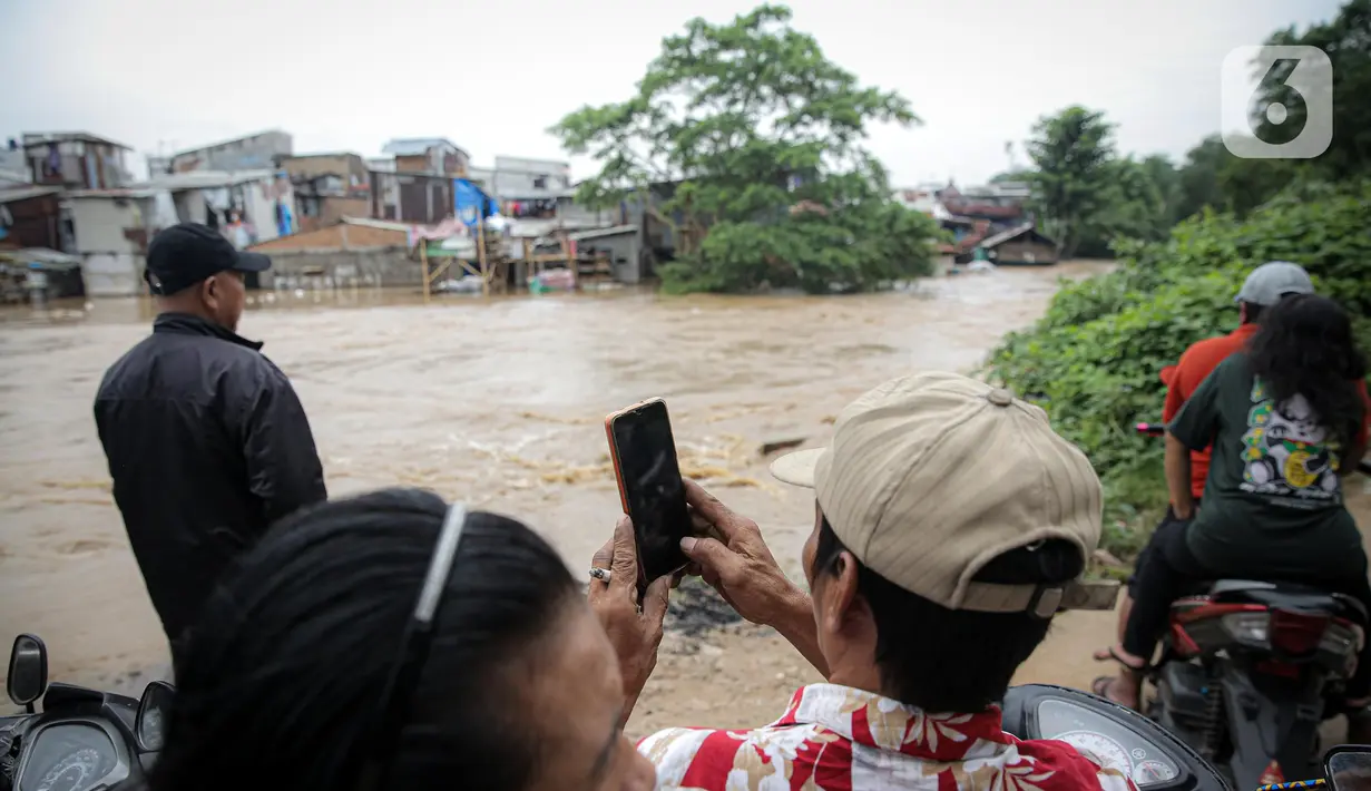 Warga menyaksikan deretan permukiman warga di bantaran Sungai Ciliwung yang terendam banjir, Jakarta, Senin (10/10/2022). Hingga pukul 09.00 WIB hari ini, Badan Penanggulangan Bencana Daerah (BPBD) DKI Jakarta mencatat sebanyak 68 RT di Jakarta terendam banjir akibat luapan Sungai Ciliwung. (Liputan6.com/Faizal Fanani)