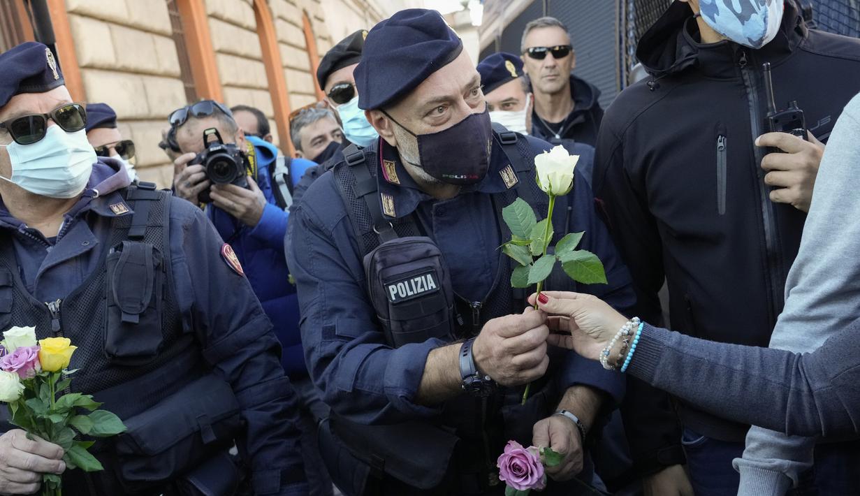 Petugas polisi menerima bunga yang diberikan demonstran selama aksi protes di Circus Maximus Roma, Jumat (15/10/2021). Protes tersebut karena aturan yang mengharuskan seluruh pekerja di Italia menunjukkan kartu kesehatan covid-19 untuk memasuki tempat kerja mereka. (AP Photo/Gregorio Borgia)