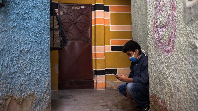 Jonathan Figueroa, 14, menggunakan ponselnya untuk terhubung ke sinyal wifi tetangga, di luar rumahnya, saat sang ibu Viviana Rodriguez mengawasinya di tengah pandemi virus corona di Bello Campo di Chacao, Caracas, Venezuela pada 6 Oktober 2020. (Cristian Hernandez/AFP)