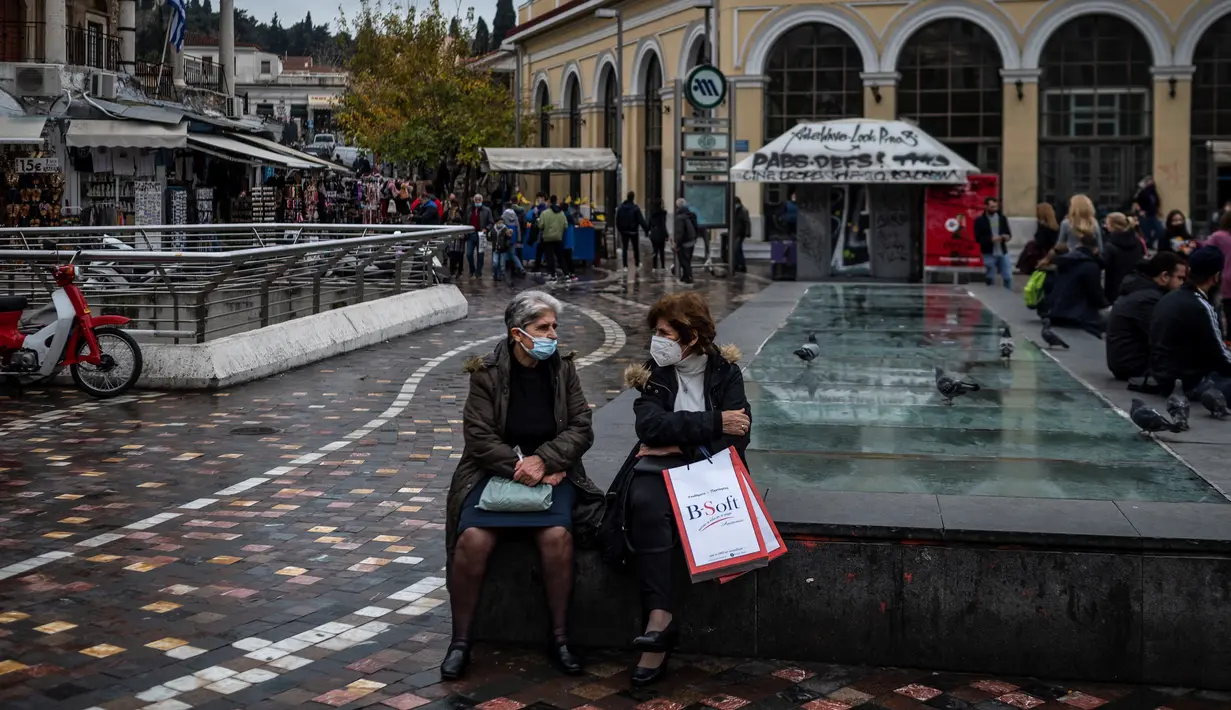 Perempuan yang mengenakan masker berbicara satu sama lain di alun-alun Monastiraki di pusat kota Athena, Yunani, Rabu (29/12/2021). Organisasi Kesehatan Dunia (WHO) memperingatkan lonjakan kasus Covid-19 varian Omicron dapat menyebabkan fasilitas kesehatan kewalahan. (Angelos Tzortzinis/AFP)