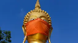 Masker diletakkan pada wajah patung Buddha raksasa di kuil Wat Nithet Rat Pradit di Pathum Thani di luar Bangkok, Thailand, 12 Mei 2020. Pemasangan masker tersebut sebagai tanggapan terhadap penyebaran pandemi Covid-19. (Photo by Mladen ANTONOV / AFP)