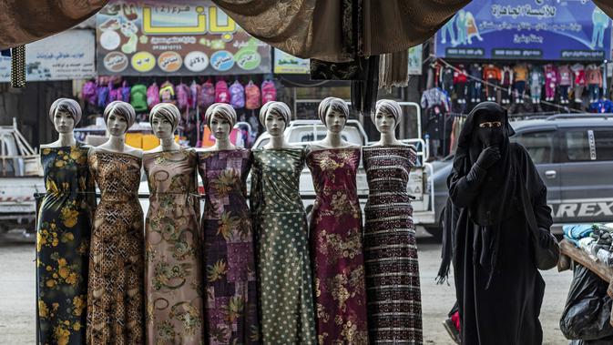 Seorang perempuan berjalan melewati boneka-boneka yang dipajang di kota Raqqa, bekas ibu kota ISIS, di Suriah utara pada 20 Desember 2020. Raqqa menjadi saksi terusirnya anggota kelompok militan tersebut oleh Pasukan Demokratik Suriah pada Oktober 2017 lalu. (Photo by Delil SOULEIMAN / AFP)